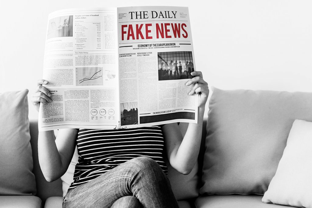 A young person reads a newspaper bearing a headline "Fake News"